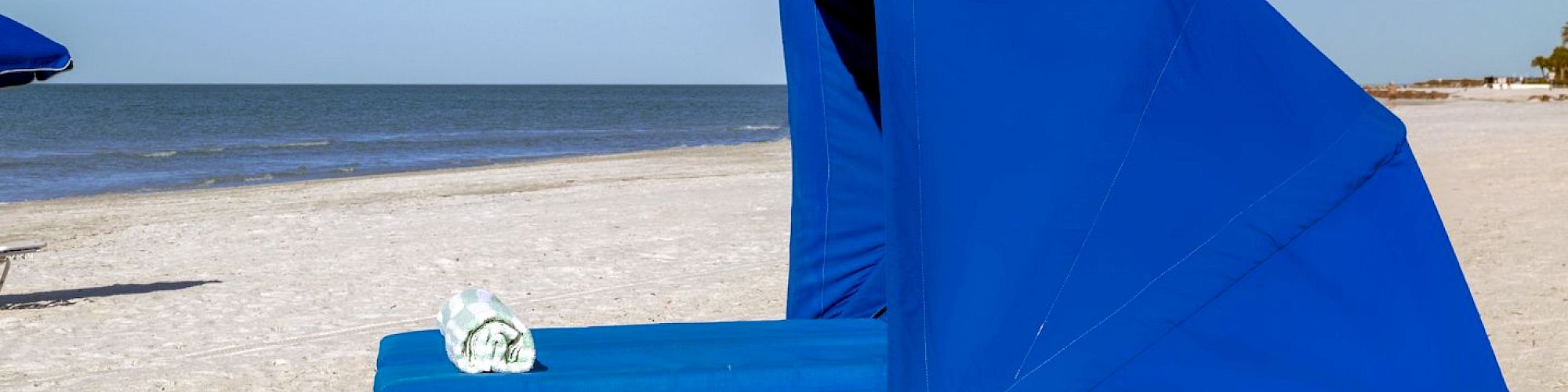 Blue beach chair with a sunshade on sandy beach, clear sky.