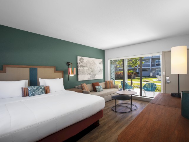Modern hotel room with a bed, sofa, artwork, and view to the outdoors.