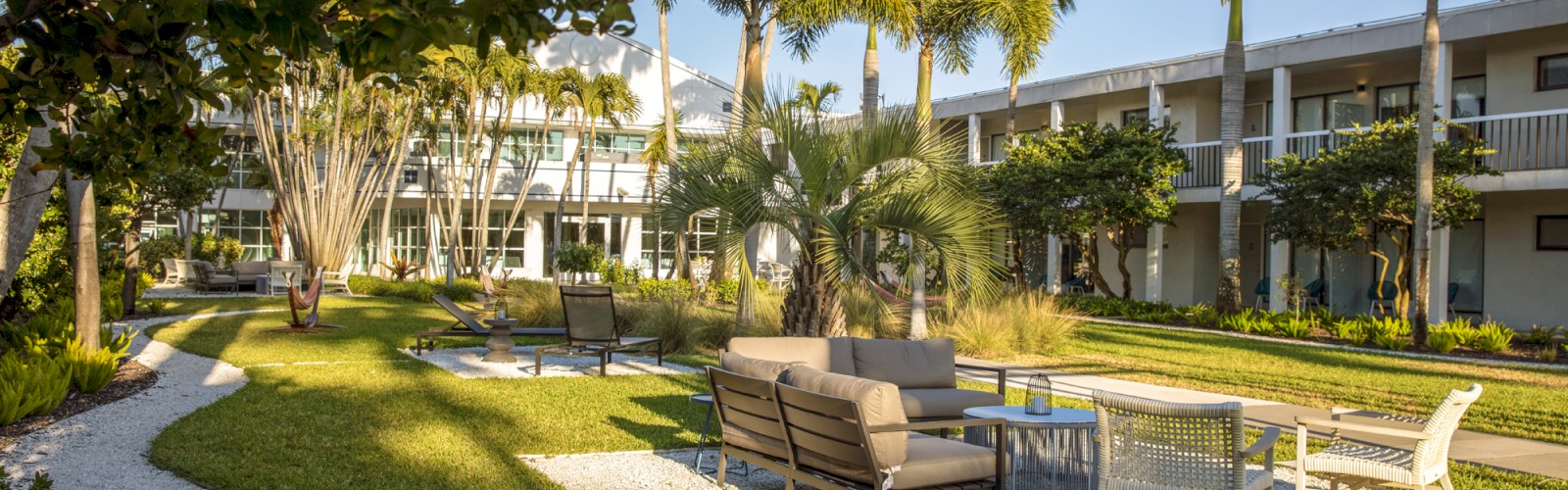 A tranquil garden with outdoor furniture, walkways, and a building in the background.