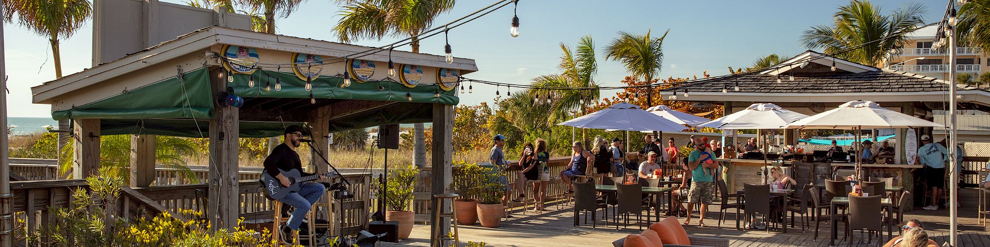 The image shows an outdoor dining area with people, furniture, and string lights.