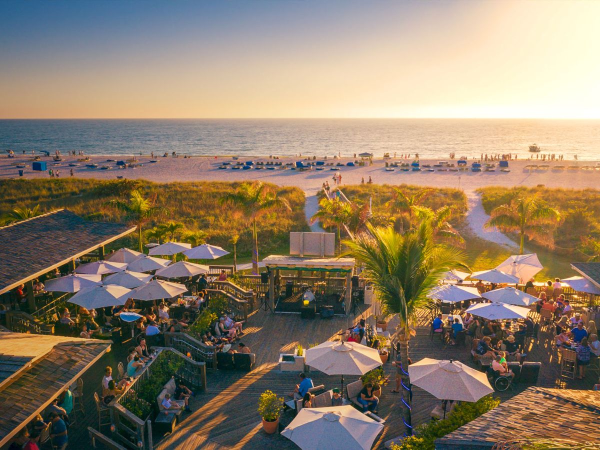 Jimmy B's on St.Pete Beach with people, umbrellas, golden sunset, and a lively atmosphere.