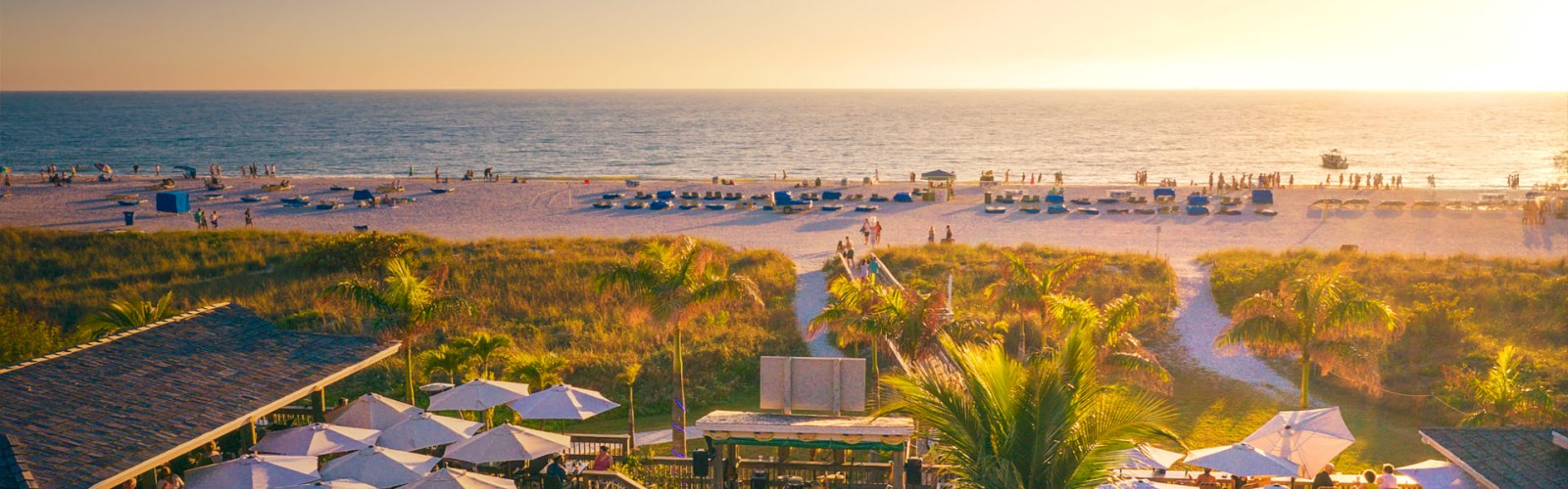 Sunset at a beachside venue with umbrellas, people, and a boardwalk.
