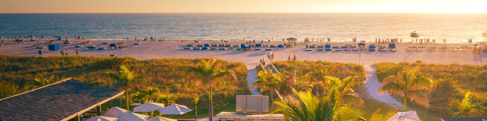 Sunset at a beachside venue with umbrellas, people, and a boardwalk.