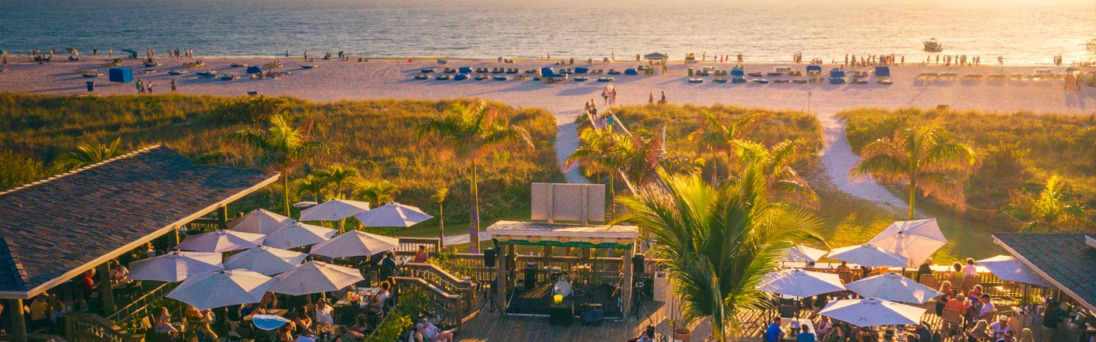 Beachside venue with people, umbrellas, sunset, and sea.