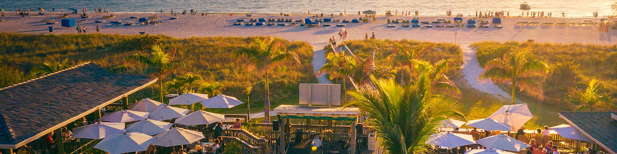 Beachside venue with people, umbrellas, sunset, and sea.