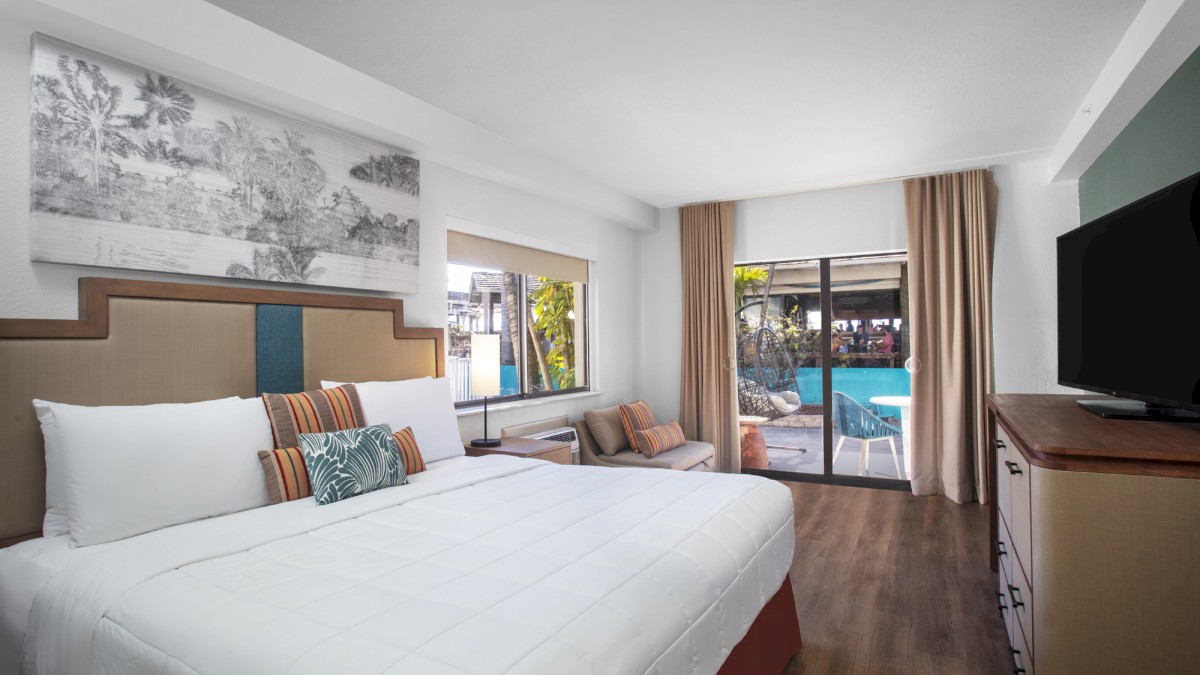 A modern hotel room with a large bed, seating area, TV, and pool view.