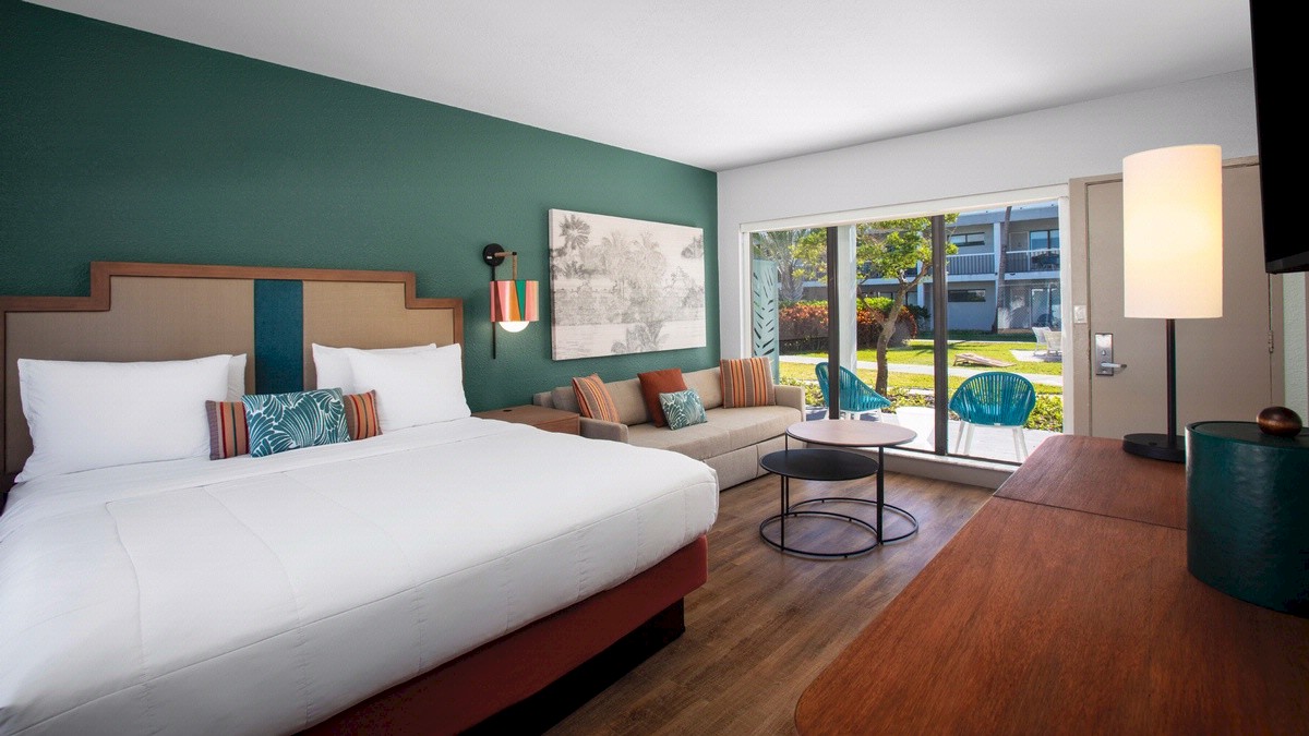 Modern hotel room with a king bed, floor lamp, seating area, and patio access.