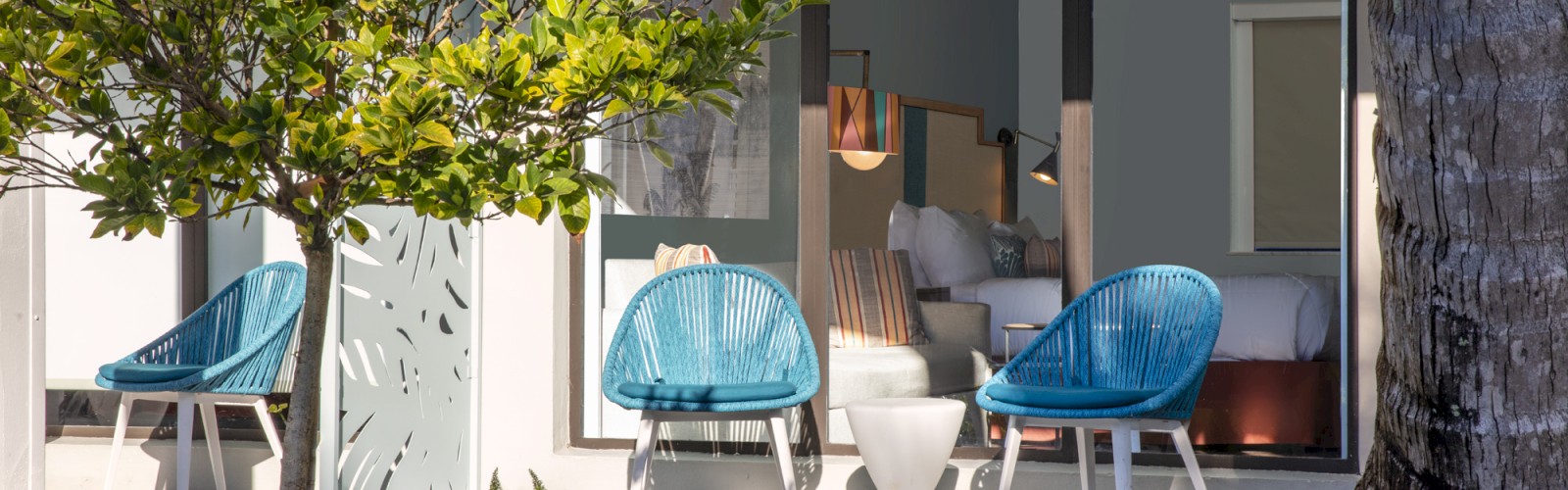 Modern terrace with blue chairs, plants, and visible interior design through glass doors.