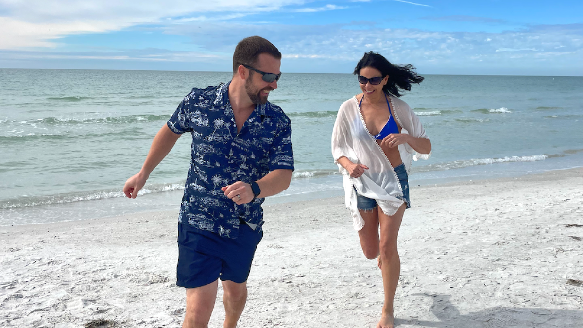 Two people are running on a sandy beach with the ocean in the background.