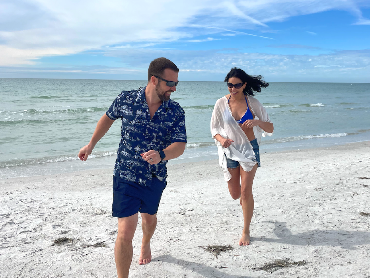 Two people are running on a sandy beach with the ocean in the background.