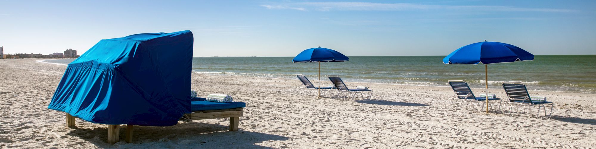 Beach scene with lounge chairs, umbrellas, and a cabana on sandy shore.