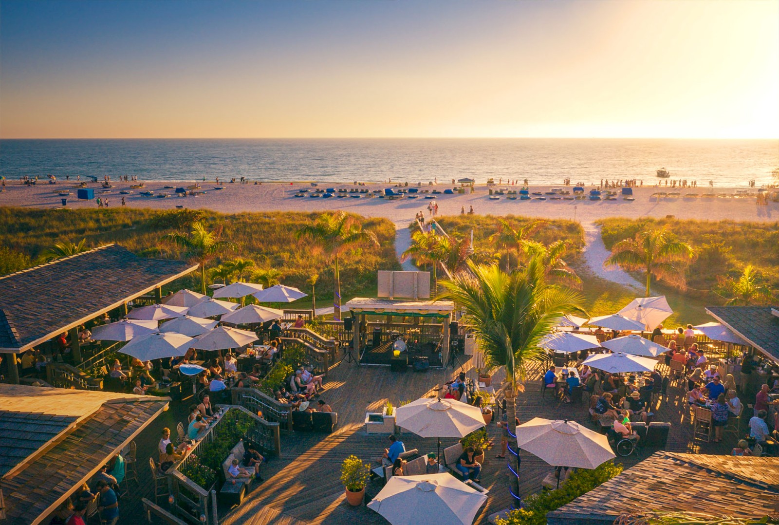Beachside venue with people, umbrellas, sunset, and sea.