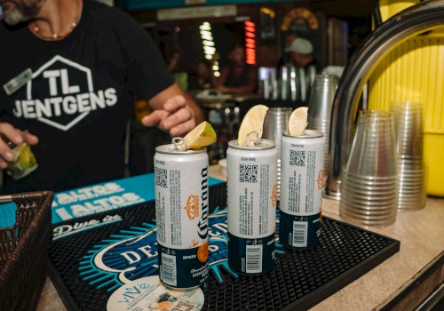 A bartender pours shots at a bar with several spray bottles of liquor and a coaster-studded counter.