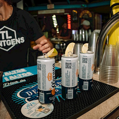 A bartender pours shots at a bar with several spray bottles of liquor and a coaster-studded counter.