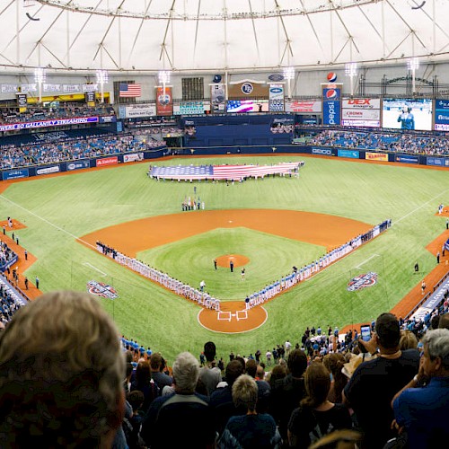 A packed baseball stadium with a large diamond, players on the field, and fans filling the stands for a game in progress.