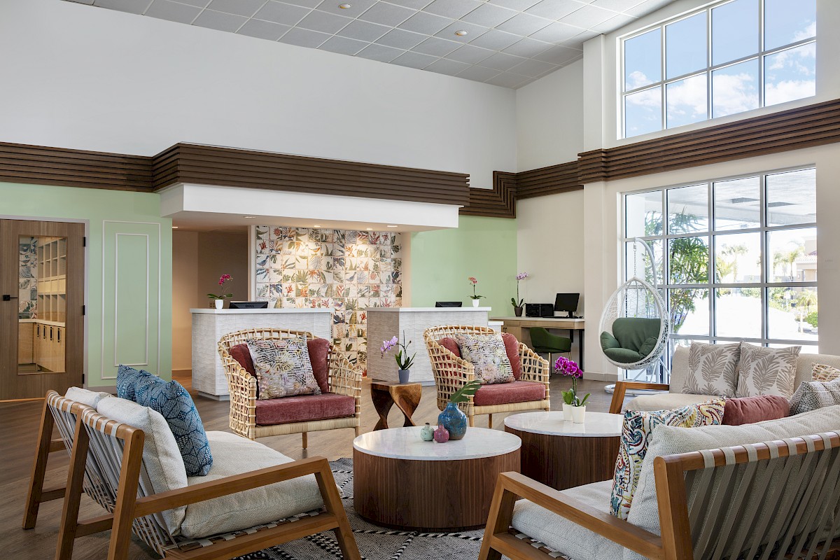 A bright, modern lobby with mid-century seating, a stone-accent reception desk, large windows, and airy, welcoming decor.