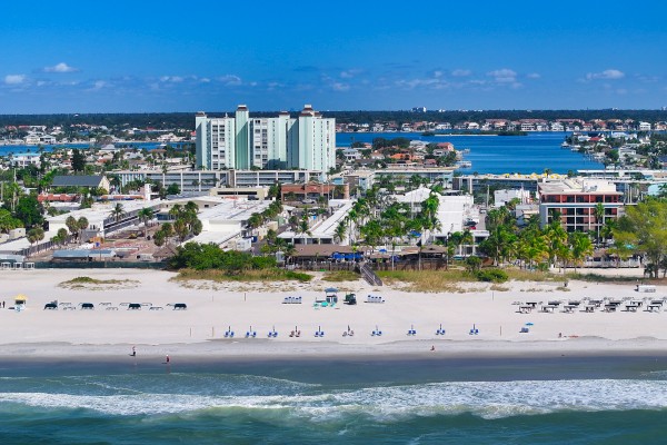 A sunny beachfront cityscape with white-sand beach, blue ocean, and high-rise hotels along the shore, overlooking calm water.